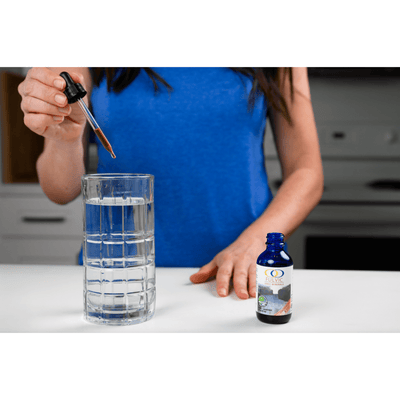Woman adding Fulvic Ionic Minerals X350 drops into a glass of water, demonstrating easy usage for daily health supplementation.